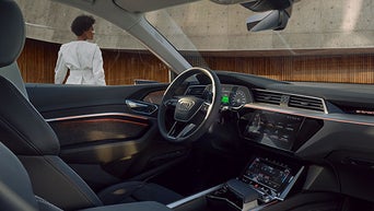 Blick ins hochwertige Interieur eines Audi Q8 e-tron; durch das Seitenfenster ist draußen eine Frau mit kurzen Haaren sichtbar.