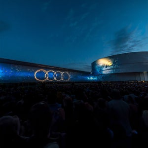Menschenmenge vor Gebäuden bei Nacht; große Projektion der Audi-Ringe auf einer Fassadenwand.
