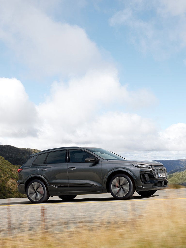 Fahrender, grauer Audi SQ6 SUV e-tron von der Seite auf Bergstraße, bei bewölktem Himmel.