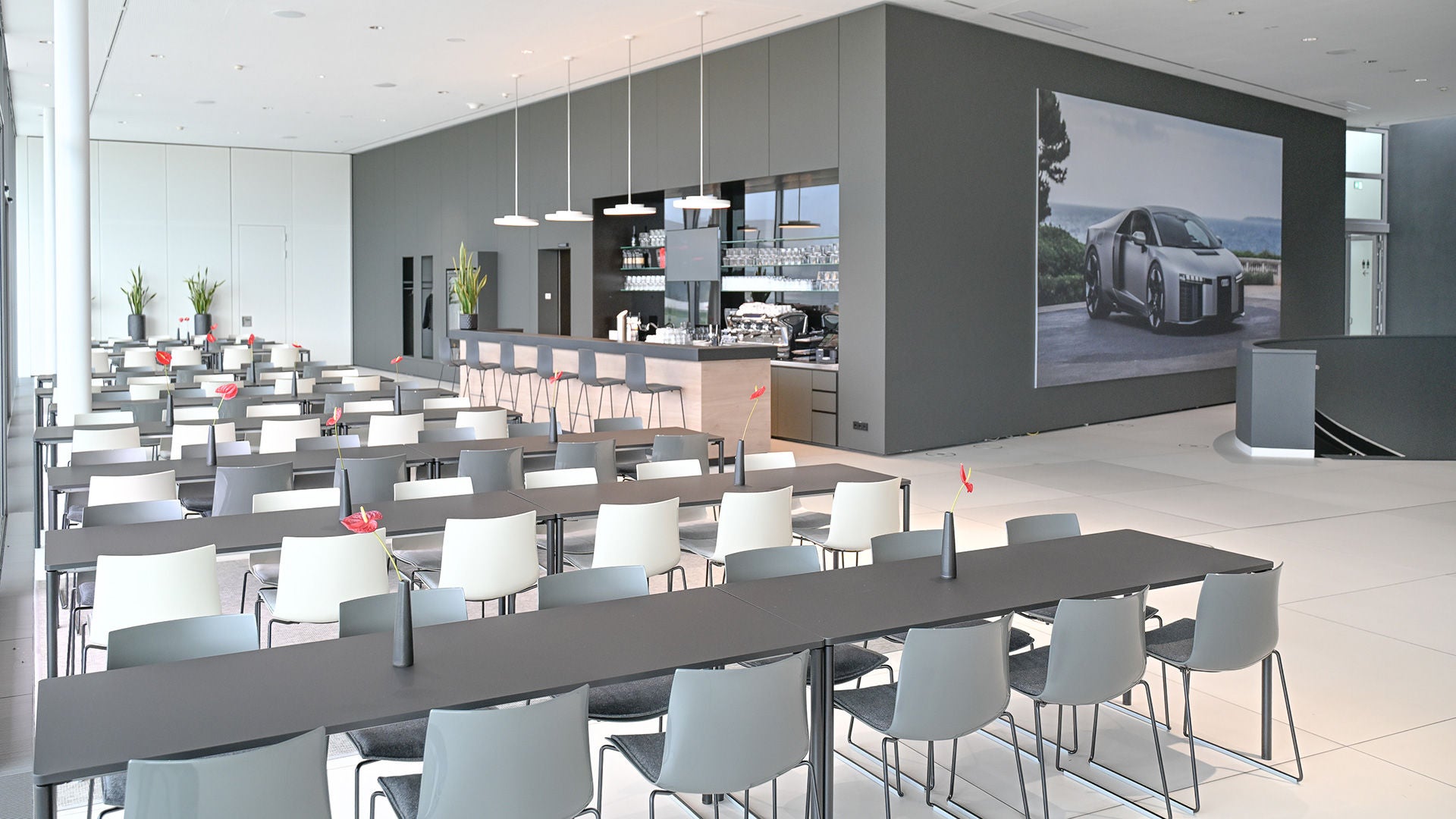 Heller Veranstaltungsraum mit Tischreihen, Bar im Hintergrund und großem Bild eines grauen Audi an der Wand.