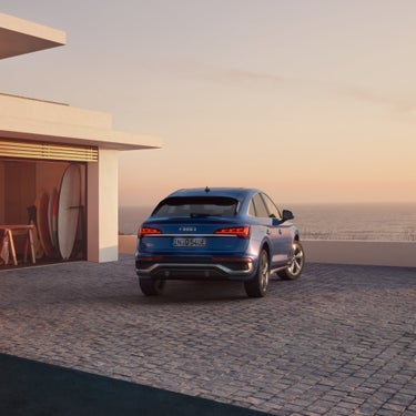 A blue Audi parked on a coastal residence driveway at sunset.