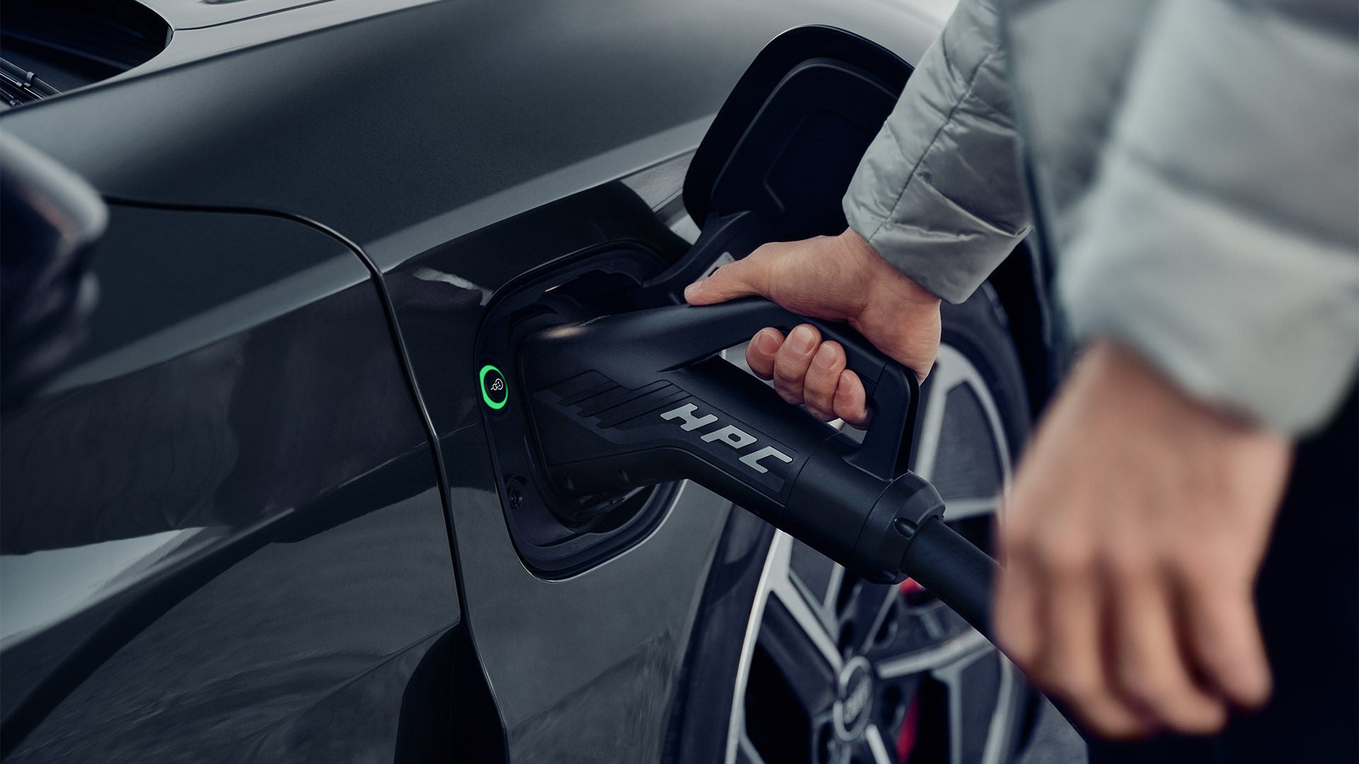 Main branchant un câble de recharge sur une voiture électrique.