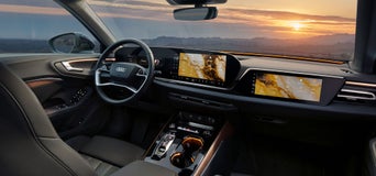 Blick ins Audi-Cockpit mit großem Display und Navigationskarte bei Sonnenuntergang.