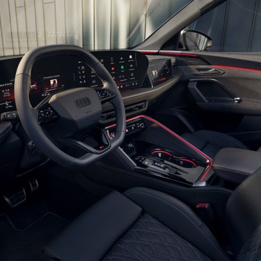 Innenraum eines Audi SQ5 Sportback mit digitalem Display und roter Ambientebeleuchtung, Fokus auf Mittelkonsole und Lenkrad.