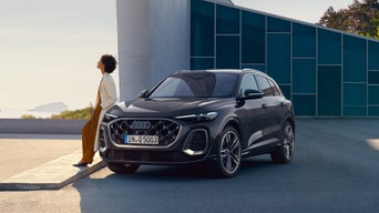 Un SUV Audi Q5 noir est garé devant un bâtiment moderne aux façades en verre bleu.