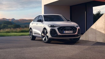 White Audi Q5 Sportback e-hybrid parked outside a modern building, surrounded by green fields and mountains in the background.