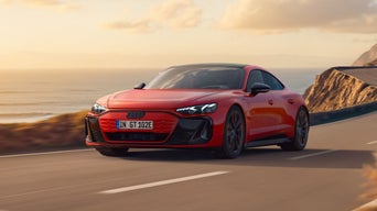 Der e-tron GT quattro fährt bei Sonnenuntergang über eine kurvige Straße entlang einer felsigen Küste.