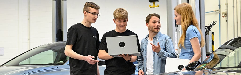 Vier Mitarbeitende von Audi sind im Gespräch und schauen sich etwas auf einem Laptop an