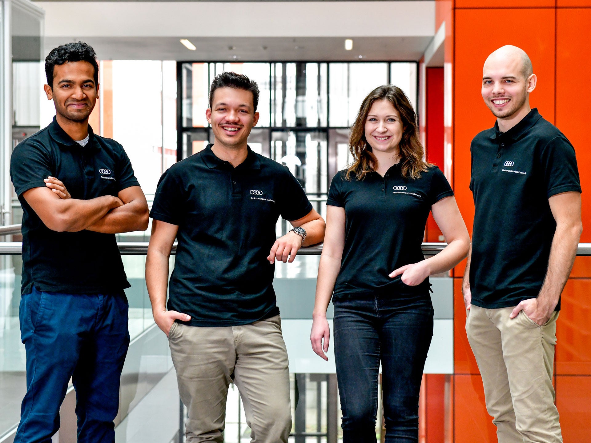 Vier Absolventen in AUDI Shirt stehen nebeneinander in einem Gang