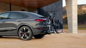 Grauer Audi SUV mit Fahrradträger steht vor modernem Gebäude.