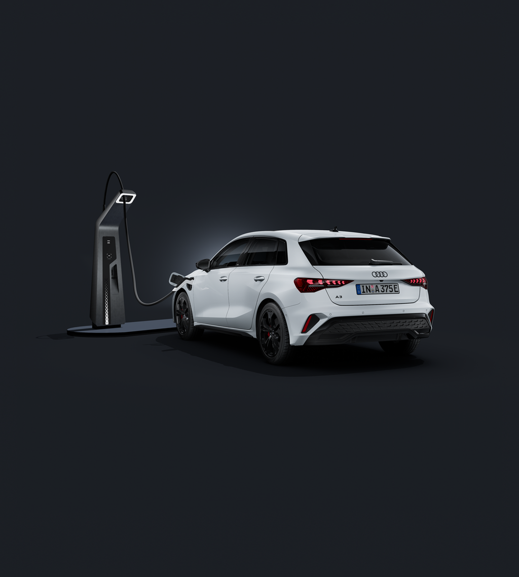 An Audi A3 Sportback e-hybrid, viewed from the rear at an angle against a dark background, connected to a fast-charging station.