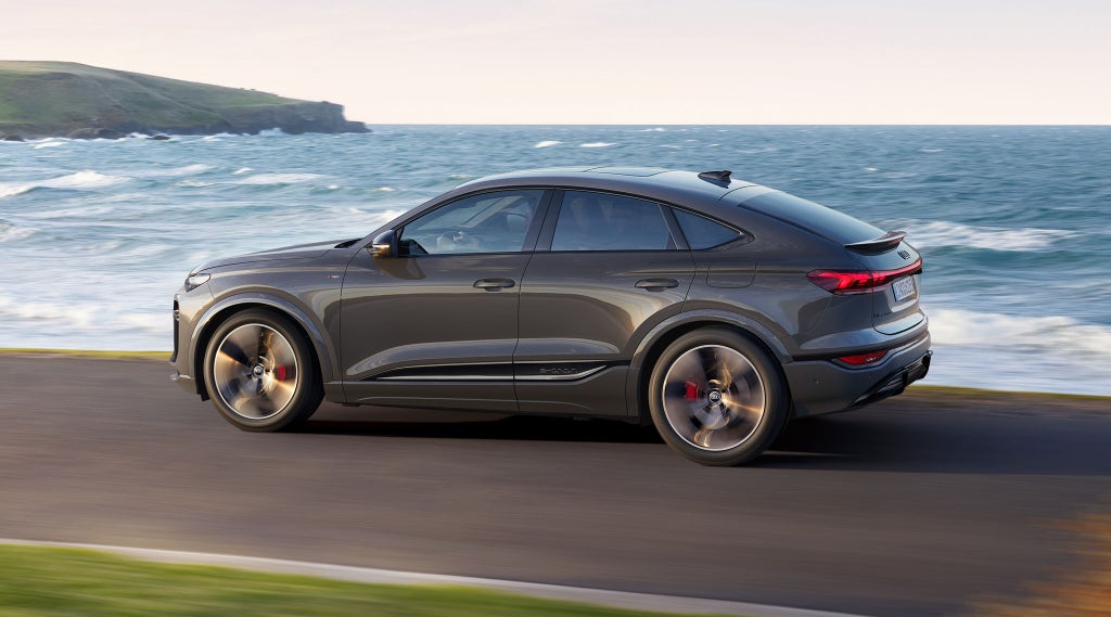 Seitliche Aufnahme des Q6 Sportback e-tron, welcher auf einer Straße entlang des Meeres fährt.