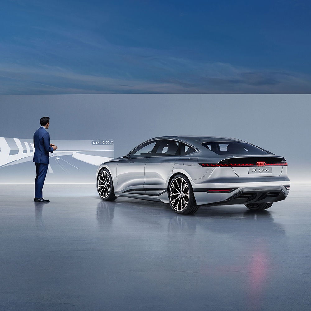 A man stands next to an Audi RS Q8 and gazes into the distance. A skyline can be seen on the horizon.