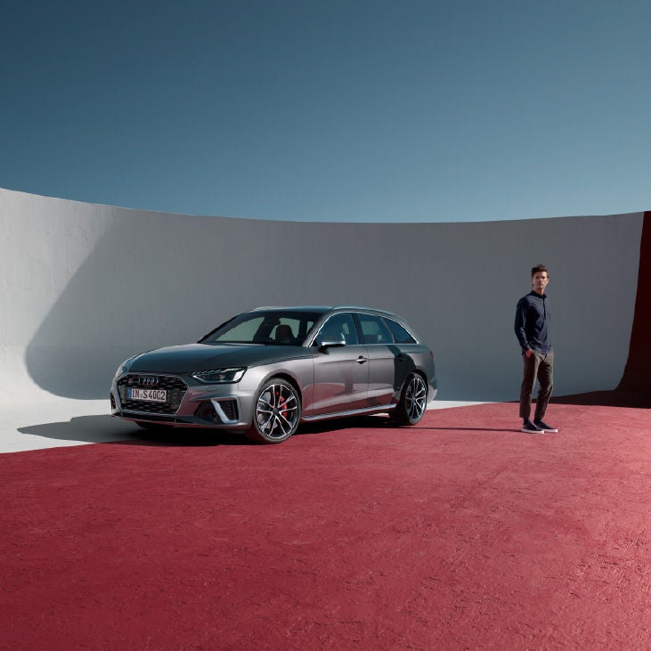 Un hombre de pie junto a un Audi sobre un suelo rojo