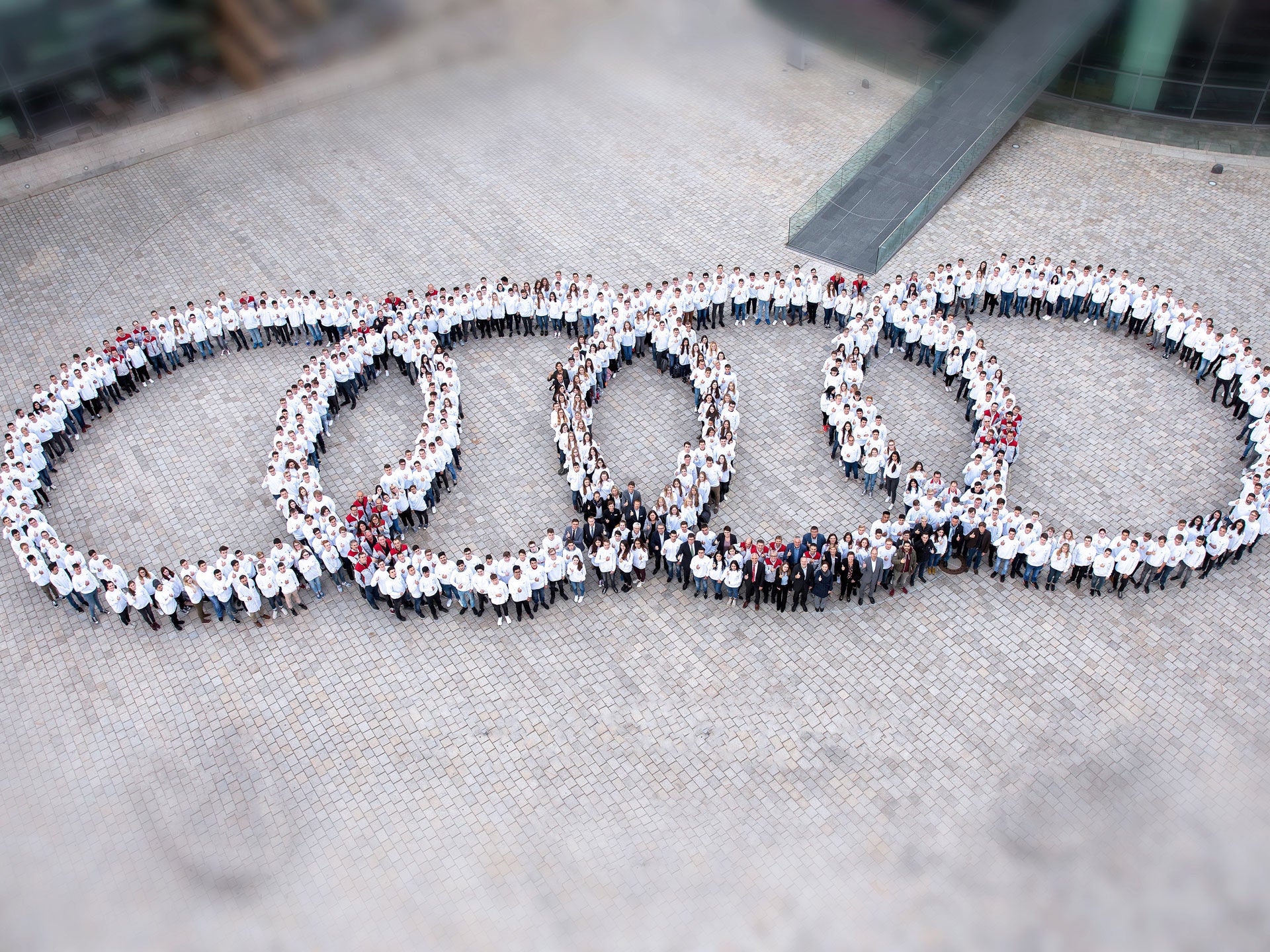 Aerial view of many Audi employees grouped together in the courtyard of the company headquarters to form the four rings.