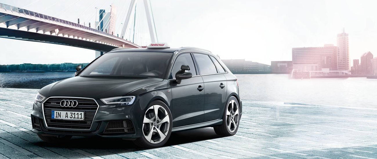 Gray Audi A3 parked on a waterfront with a bridge in the background and a "RADIO PERMIT" sign above.