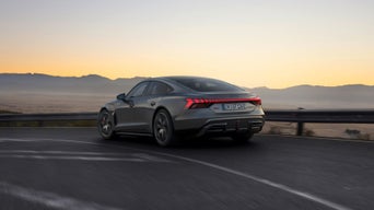 An Audi RS e-tron GT car driving on a highway in the early evening with a clear sky and mountains in the background