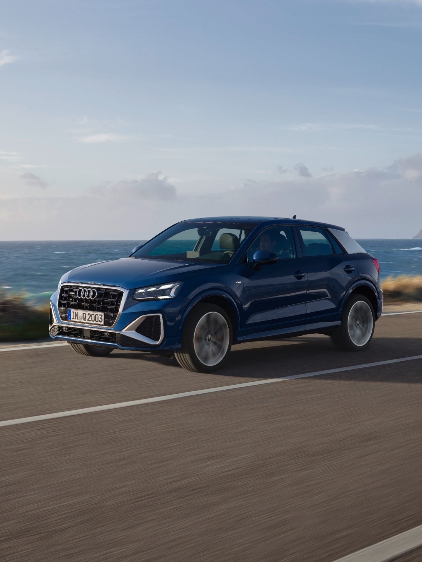 Blue Audi SUV driving along coastal road with sea and cliffs in the background.