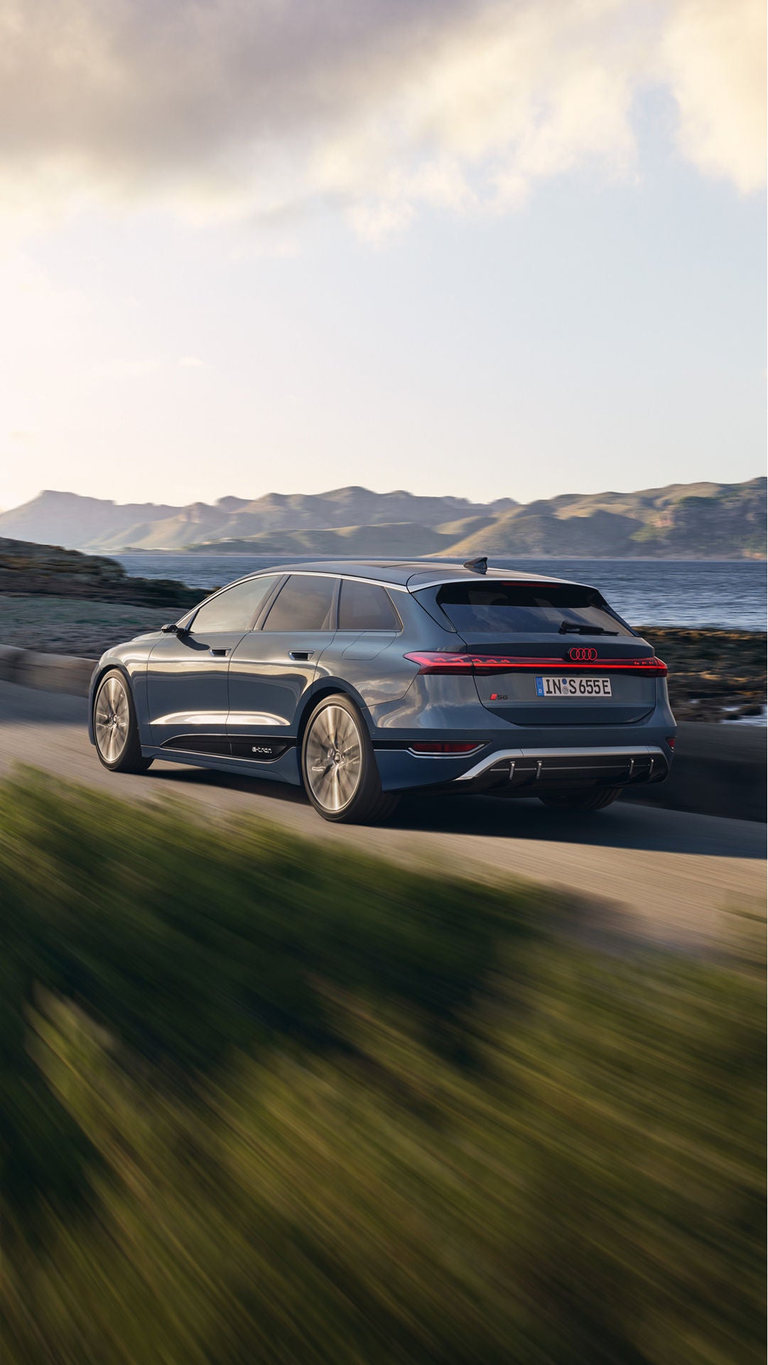 Car driving along a coastal road with mountains in the distance.
