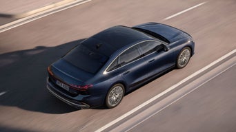 A sleek blue Audi sedan speeds along a smooth road, showcasing its elegant design and modern silhouette from an aerial view.