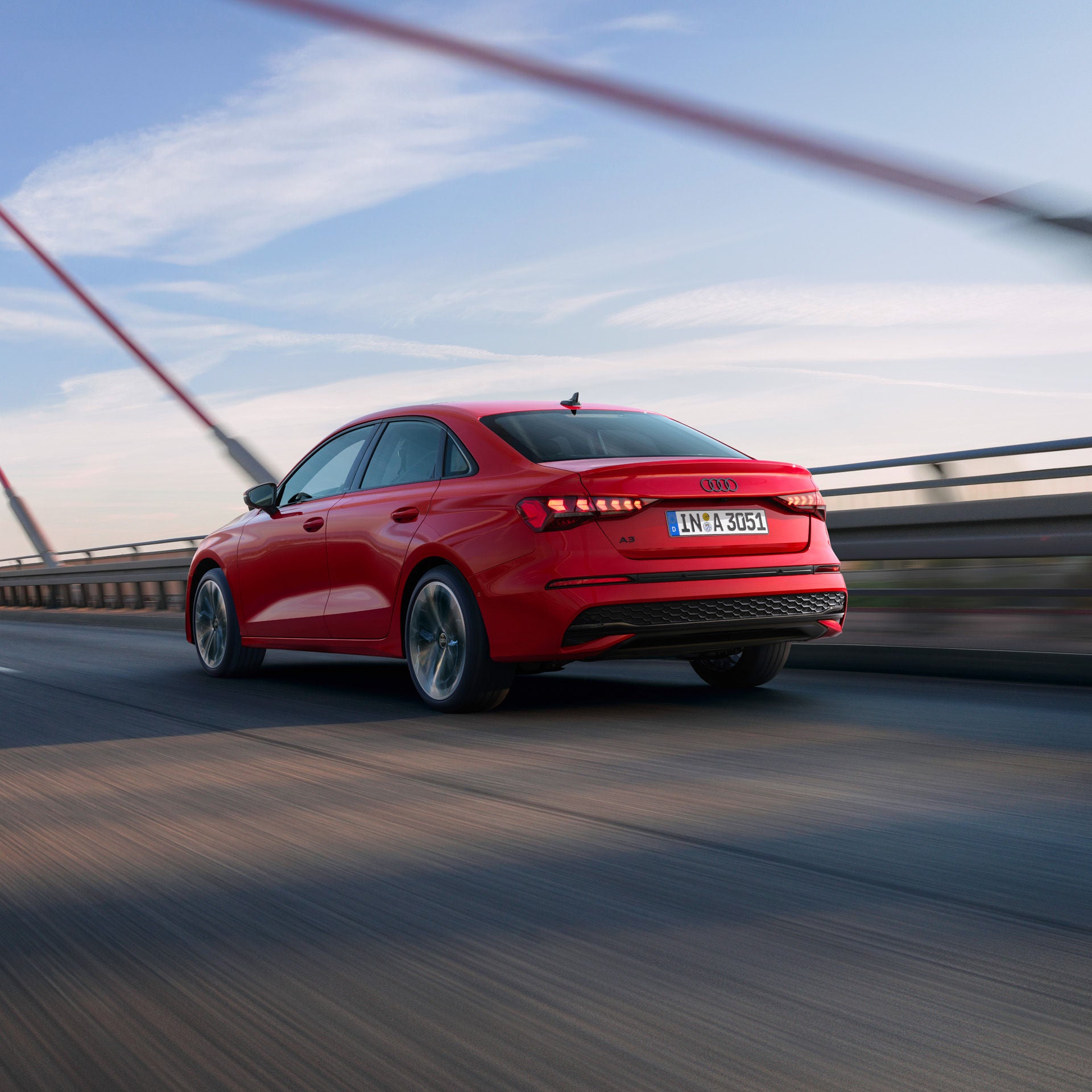 Rote Audi A3 Limousine fährt über eine Brücke, aufgenommen von schräg hinten bei Tageslicht.