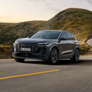Seitliches Frontprofil des SQ6 SUV e-tron, welcher über eine Landstraße in bergiger Umgebung fährt.