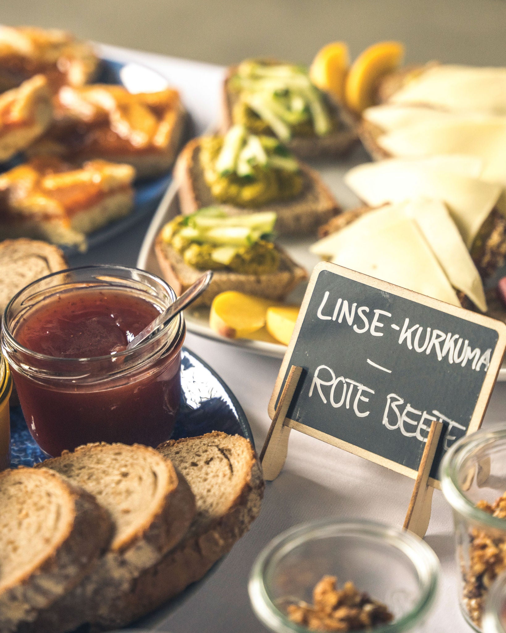 Tisch mit belegten Broten, Marmelade und Schild 'Linse-Kurkuma – Rote Beete'.