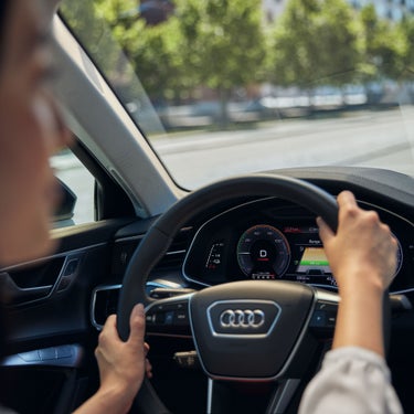 Blick auf das digitale Cockpit eines Audi, Hände am Lenkrad, Anzeige zeigt Fahrmodus, Reichweite und Geschwindigkeit.