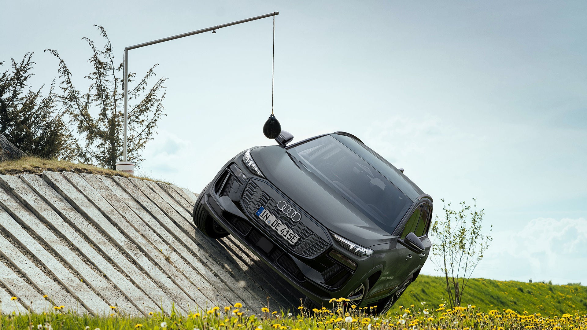 Ein schwarzer Audi SQ6 SUV e-tron fährt schräg über eine geneigte Betonrampe in einem Offroad-Testgelände mit Messpendel.