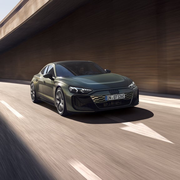 Grüner Audi RS e-tron GT performance fährt unter einer Betonbrücke auf einer mehrspurigen Straße mit Bewegungseffekt.