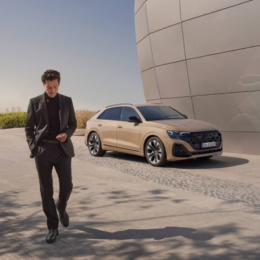 Man walking away with Audi Q8 parked behind infront of architecture and skyline.