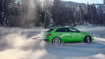 A light green Audi RS 3 Sportback is drifting in the snow.