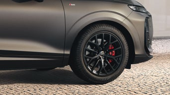 Nahaufnahme des Vorderrads eines Audi-Autos mit schwarzen Felgen und roten Bremssätteln.