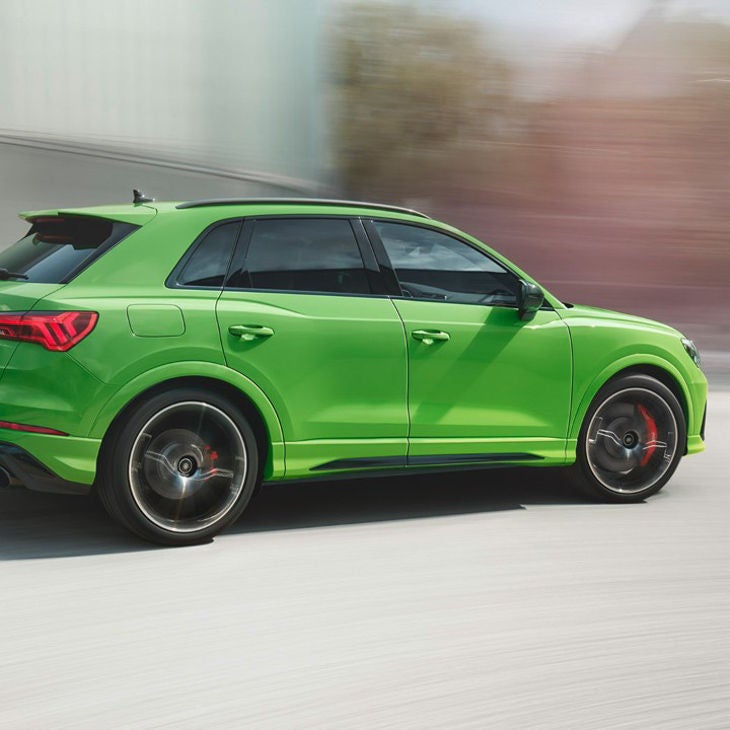 Side view of green Audi Q3 RS with blurred background.