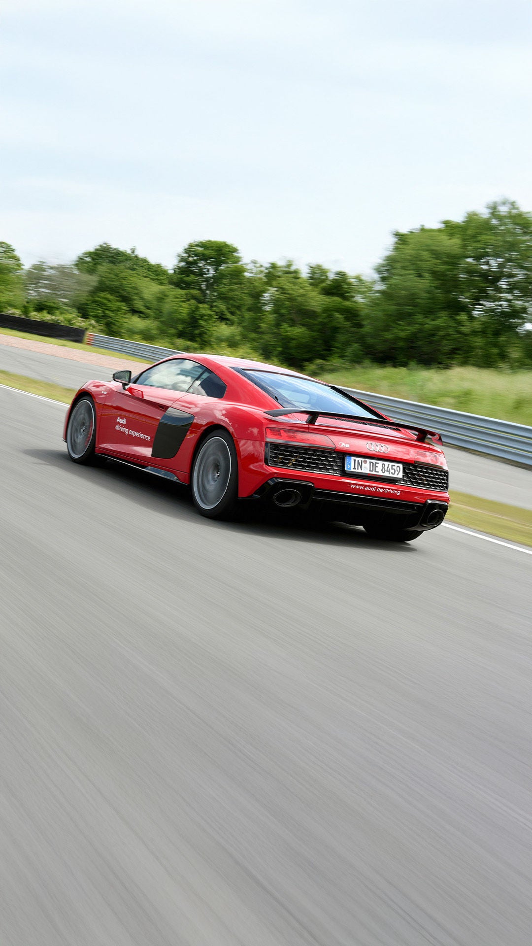 Red Audi R8 Coupé V10 performance quattro driving on a race track, photographed from the rear left.