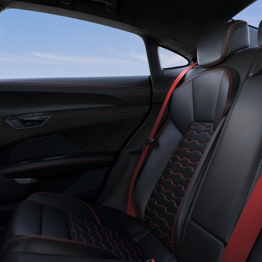 Black leather car seats with red stitching and trim, viewed from the side, with a blue sky visible through the window.