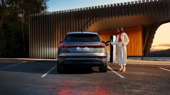 A dark colour SUV charging at an electric vehicle station during sunset.