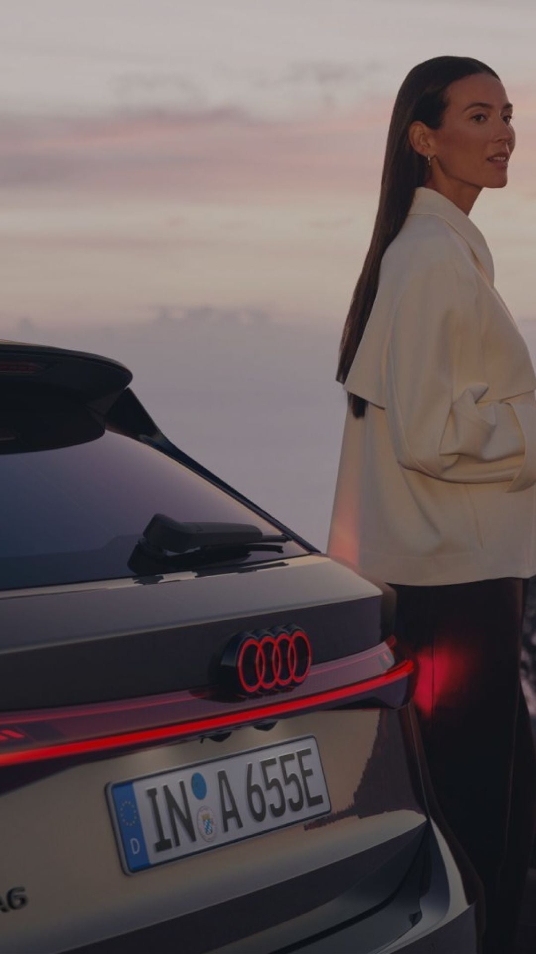 A person standing next to an Audi car at dusk with a soft sky background.