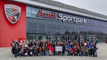 Eine Gruppe Audianer und Vertreter regionaler Sportvereine posiert vor dem Haupteingang des Audi Sportparks in Ingolstadt