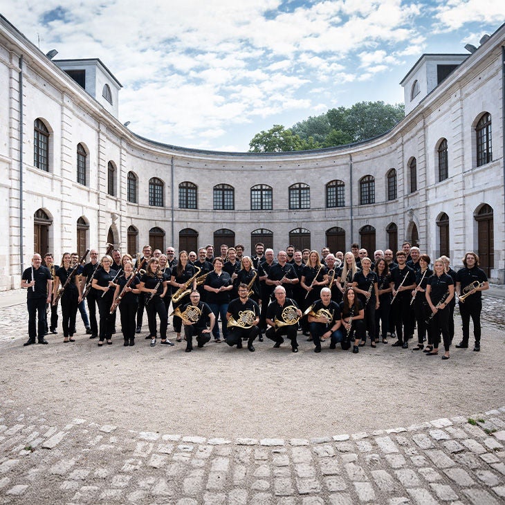 Gruppe der Audi Bläserphilharmonie steht im Innenhof eines hellen, historischen Rundbaus.