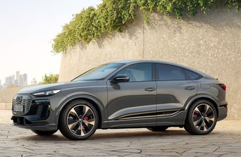 A sleek grey Audi SUV parked on a stone surface, highlighted by urban skyline in the background and greenery above.