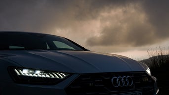 Frontansicht eines Audi mit leuchtenden Matrix-LED-Scheinwerfern vor dunklem, wolkenverhangenem Himmel.