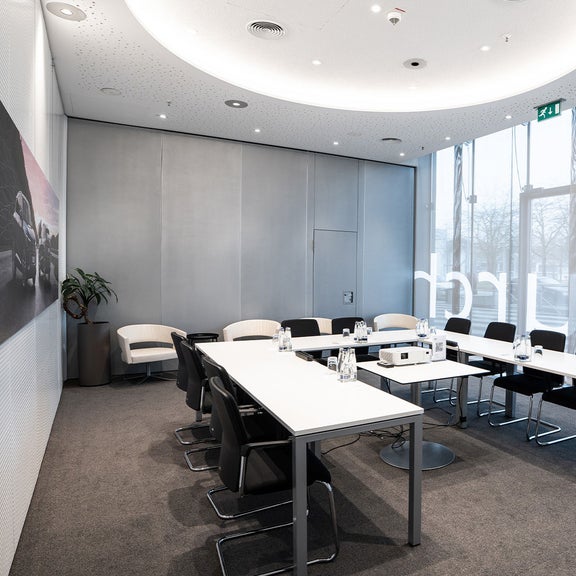 Konferenzraum mit U-förmig gestellten Tischen, Stühlen und Getränken auf dem Tisch.