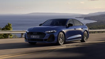 The S5 Avant with its sloping rear profile as it drives toward a city on a road.&nbsp;