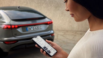 A man is looking at his phone screen. An Audi model is parked in the background.