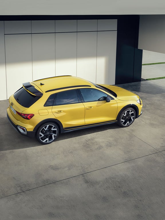 Gelber Audi A3 allstreet von schräg oben rechts auf Betonboden vor heller Gebäudewand geparkt.