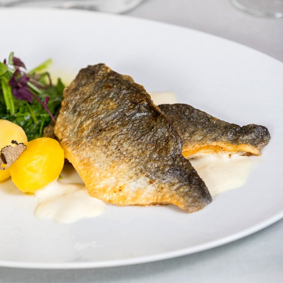 White plate with potatoes, green salad and fish in a light sauce.