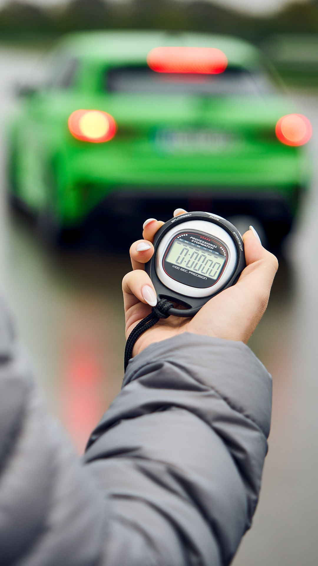Jemand hält eine Stoppuhr in der Hand, im Hintergrund befindet sich ein hellgrünes Audi Modell.