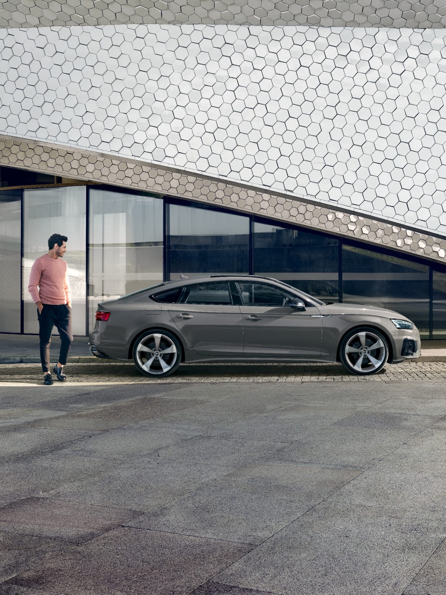 A grey Audi A5 Sportback parked outside a modern building with hexagonal patterns.