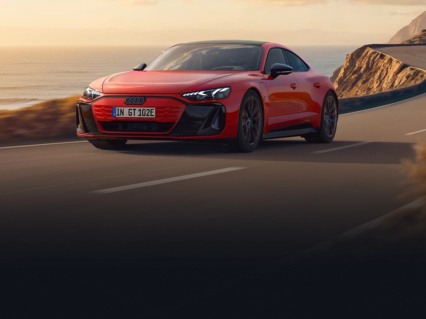 Red Audi e-tron GT driving along a coastal road with the sea and cliffs in the background